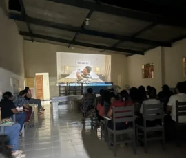Foto de uma sala com cadeiras de madeira e uma plateia assistindo ao filme "uma mulher comum".